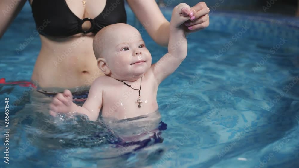 The little infant learns to swim in the pool with his mother. The little infant learns to swim in the pool with his mother.
