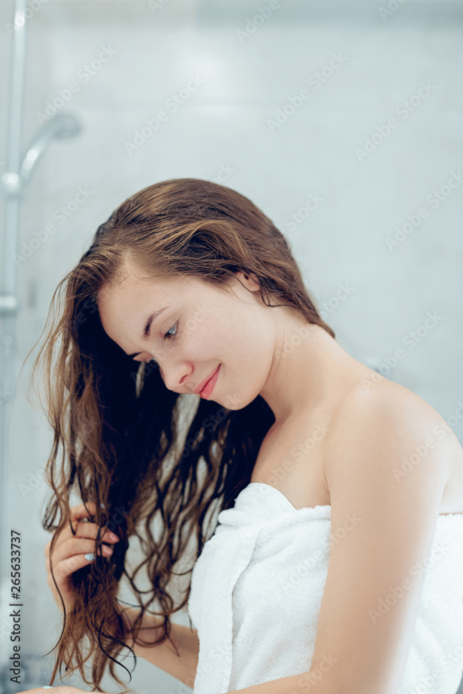 Fototapeta premium Portrait Of Beautiful Young Female Model in Bath Applying Hair Oil. Closeup Of Sexy Woman In Towel Drying Wet Long Hair. Health And Beauty Concept. Protection moisturizing cream.