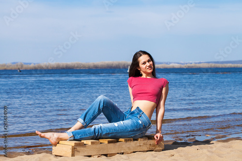 Portrait of a young beautiful woman in trendy jeans posing against the backdrop of the Volga River