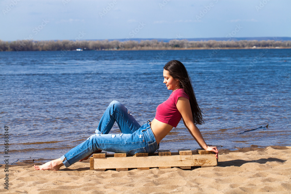 Portrait of a young beautiful woman in trendy jeans posing against the backdrop of the Volga River