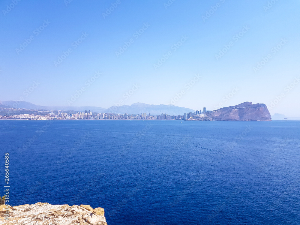 View from the island of Benidorm, Spain. Image of the view from above with all the Mediterranean Sea and the skyline and beaches of Benidorm and low scrub and rock in the foreground.