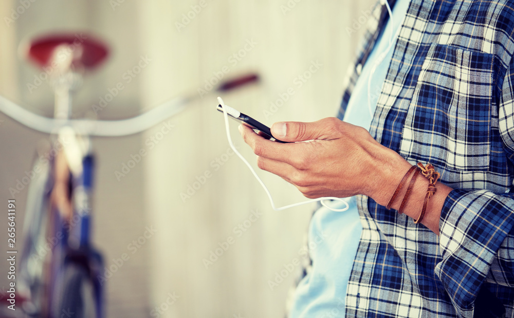 people, technology, leisure and lifestyle - close up of young hipster man with earphones, smartphone and bicycle listening to music