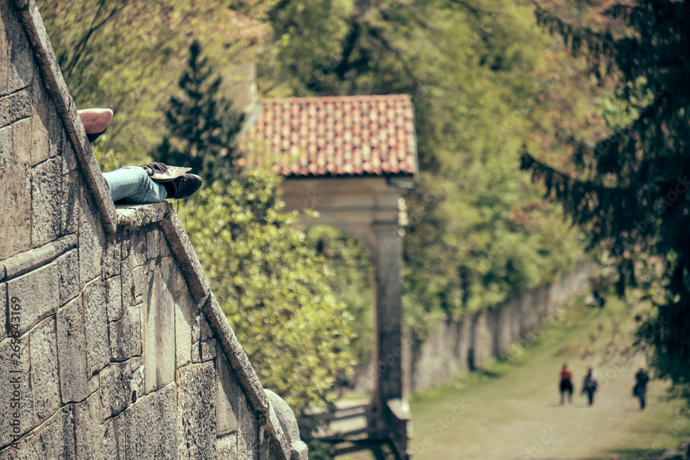 senior woman taking rest and sun along the path of the historic pilgrimage route from Sacred Mount or Sacro Monte of Varese, Italy