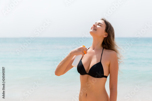 Brown hair woman is applying sunsceen from the spray on her body at the sea background