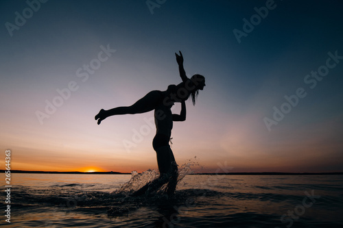 Couple kissing on the beach with a beautiful sunset in background, man lifting the woman