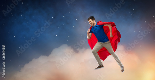 super power and people concept - happy young man in red superhero cape flying in air over starry night sky background