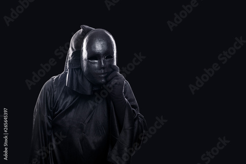 Scary figure in hooded cloak with mask in hand isolated on black background