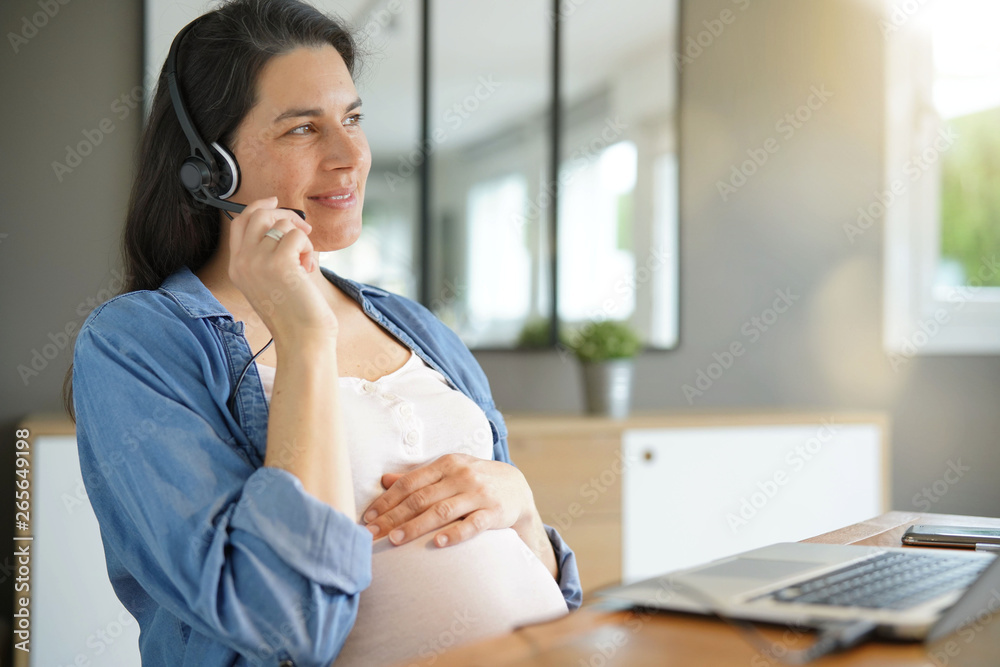 Pregnant woman working from home with laptop and headset Pregnant woman working from home with laptop and headset