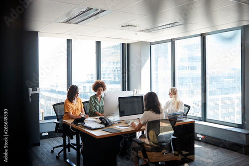 Four female creative colleagues working together in an office, seen through glass wall