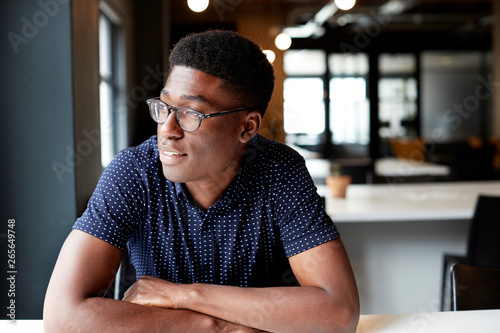 Millennial black male creative sitting at a desk in an office looking out of the window, close up