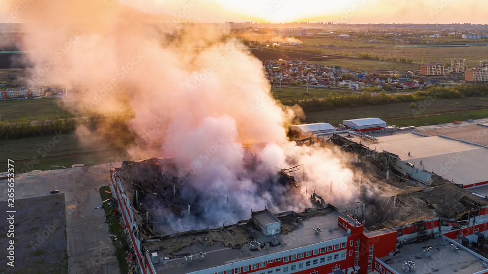 Aerial view of burnt industrial warehouse or logistics center building after big fire with huge smoke from burned roof