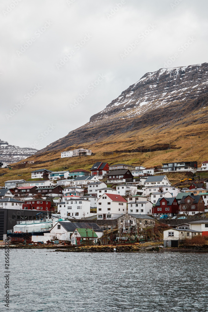 Picturesque colourful houses in the small town Klaksvík in front of snow-covered mountains as seen from a ferry towards Kalsoy island and Kallur lighthouse (Faroe Islands, Denmark, Europe)