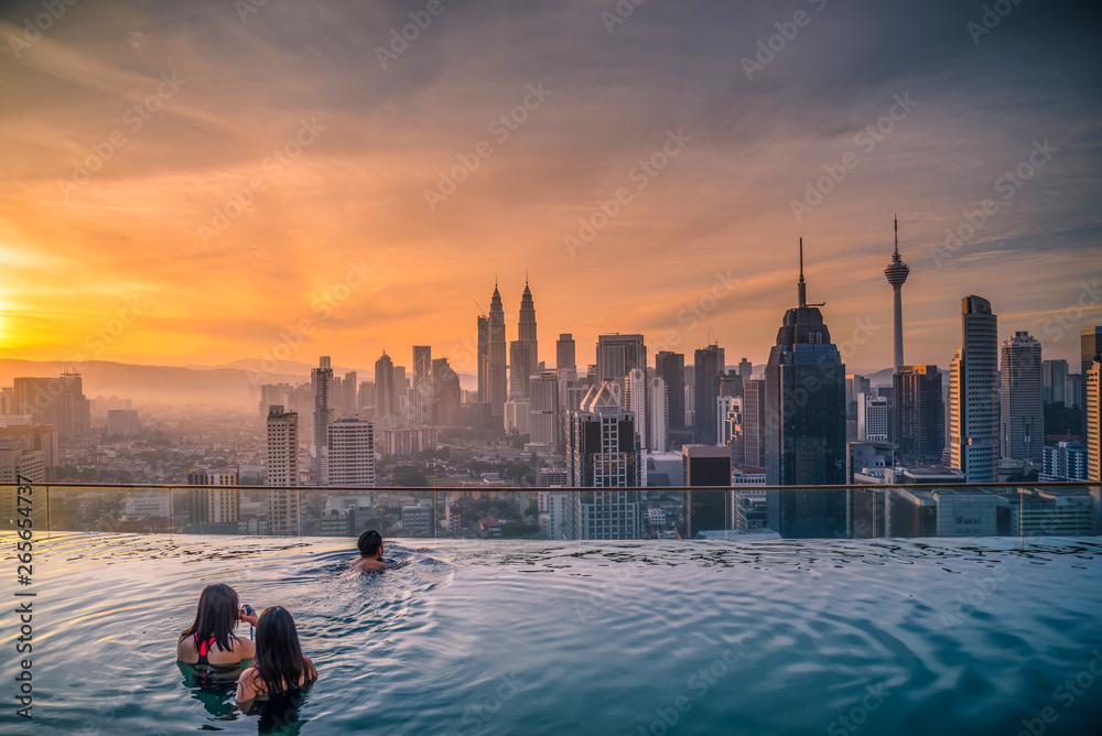 Naklejka premium Podróżujący patrząc na panoramę miasta Kuala Lumpur w basenie na dachu hotelu o wschodzie słońca w Kuala Lumpur, Malezja.