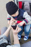 Baby boy in sitting stroller touching mobile smart phone in moms hand, lifestyle stock photo image