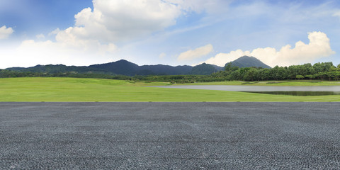 Panoramic empty concrete floor and green grass in beautiful park under the blue sky