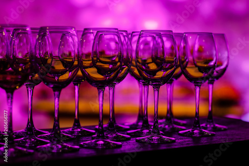 Stemware in purple light. Many glass of wine on a table. Glasses with wine. Filled with half and stand on the holiday table. Furshet. selective focus