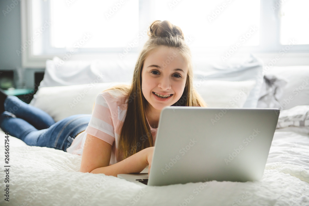 A Young smiling teen girl on bed with laptop A Young smiling teen girl on bed with laptop