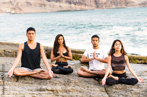 fitness, sport, yoga and healthy lifestyle concept - group of people meditating in lotus pose over exotic tropical beach background