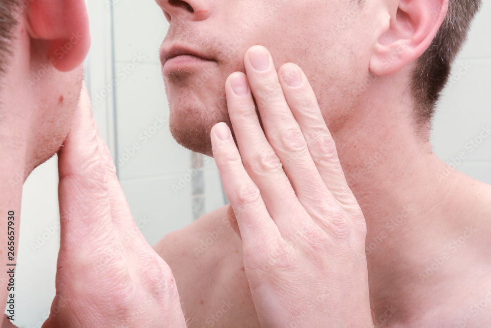 Man looking in mirror and applying product to skin on face in the bathroom