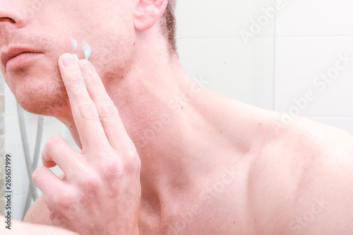 Man looking in mirror and applying product to skin on face in the bathroom