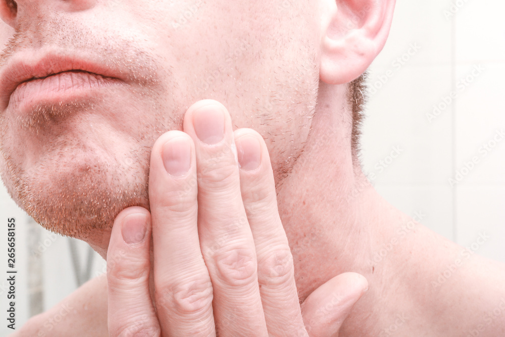 Man looking in mirror and applying product to skin on face in the bathroom