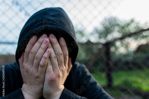 Tableau sur toile Frustrated teenage boy covering hes face in front of correctional institutes wired fence, conceptual image of juvenile delinquency , shallow depth of field, copy space