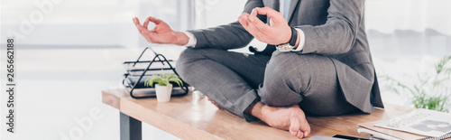 panoramic shot of businessman meditating in Lotus Pose on office desk