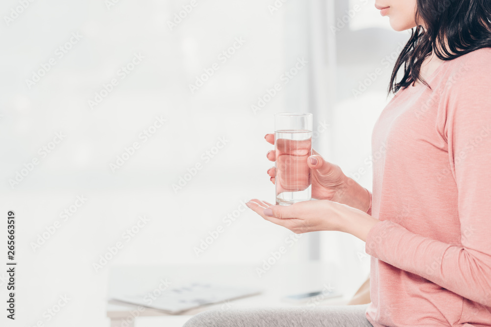 Cropped view of woman holding glass of water at home with copy space Cropped view of woman holding glass of water at home with copy space