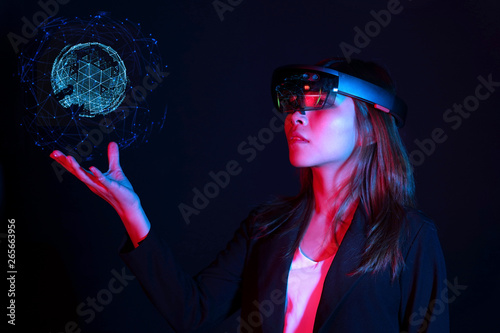 Business woman try vr glasses hololens in the dark room. Young asian girl experience ar with glow earth globe on hand. Future technology concept