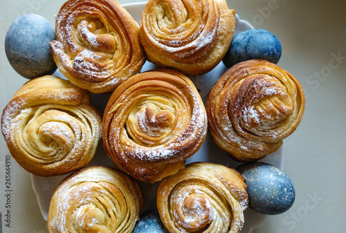 Sweet buns covered with icing sugar. And chicken eggs painted blue. Easter dish.