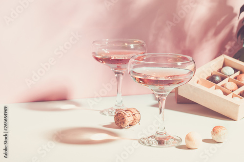Champagne or wine in glasses box of chocolates of white and dark chocolate on pink background bright light. Copy space.