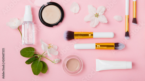 Face care and make up products with spring apple bloom (tonic or lotion, serum, cream, micellar water, cotton pads and makeup brushes) on pink background. Freshness and face care. Decorative cosmetics