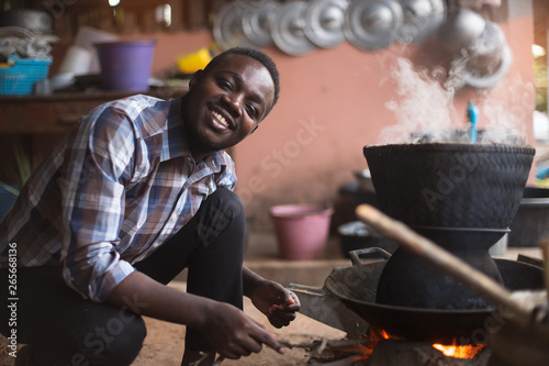 African man sitting to blow fire to cook rice photo