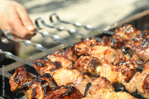 Meat skewers on grill and man hand as background, closeup. Outdoor kitchen
