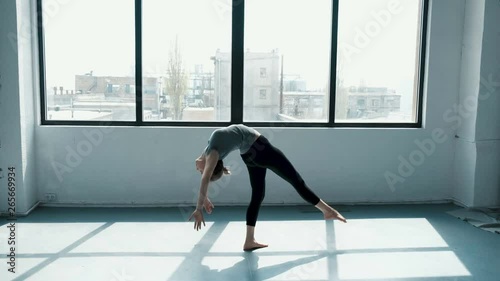Young female performs a backflip with hands in the dance stodio Flexible woman doing splits in fashion look. View on window sunny day