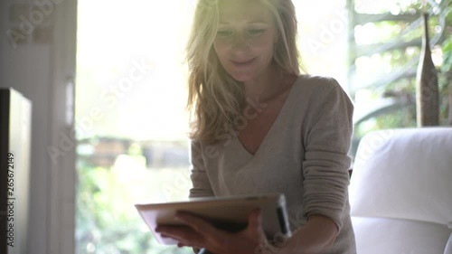 Medium shot of a mature woman using a digital tablet while relaxing on the sofa at home