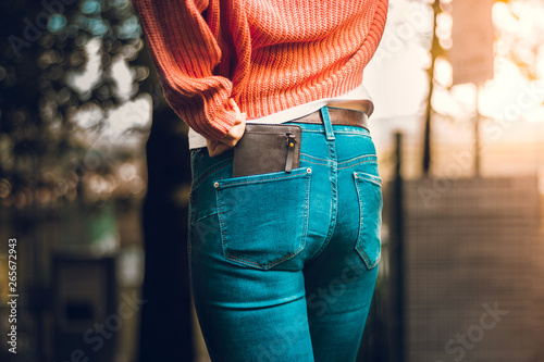 View from behind of a woman wearing tight jeans and an orange blouse with a brown leather wallet placed in the back pocket – Concept image for savings and finances photo