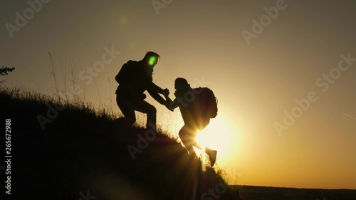 traveler man extends his hand to a girl climbing to the top of hill. travelers climb the cliff holding hand. teamwork of business people. Happy family on vacation. tourists hug on top of mountain