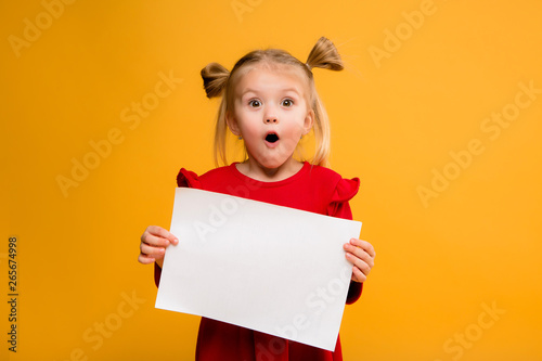 baby girl holding white sheet.Cute little girl with white sheet of paper.yellow background.copy spase.Little girl holding empty sheet of a paper photo