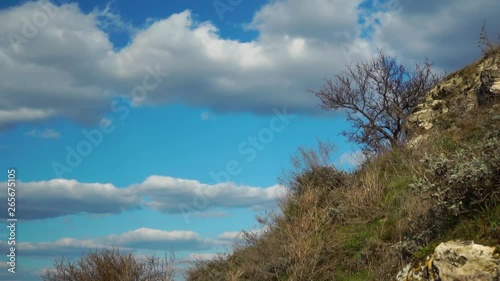 White puffy clouds floating slowly in clear blue sky under wild nature hill on bright spring day