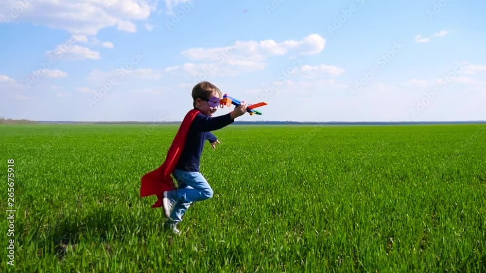 A happy child imagines a superhero and runs across the green grass, holding the plane. Joyful boy playing outdoors A happy child imagines a superhero and runs across the green grass, holding the plane. Joyful boy playing outdoors