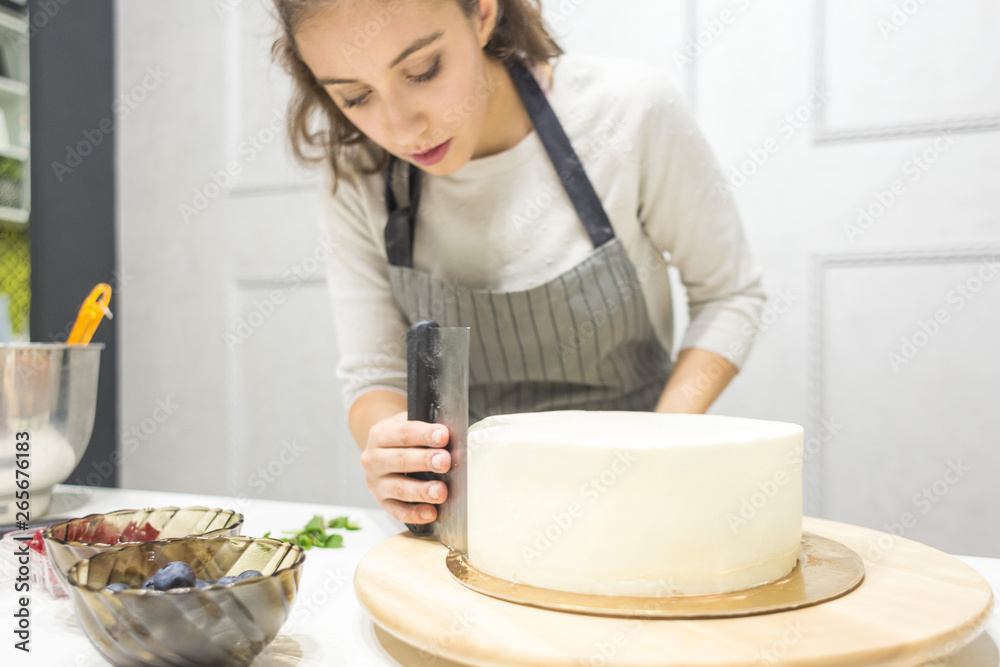 Confectioner smooths white cream on a biscuit cake with a cooking spatula. The concept of homemade pastry, cooking cakes. Confectioner smooths white cream on a biscuit cake with a cooking spatula. The concept of homemade pastry, cooking cakes.