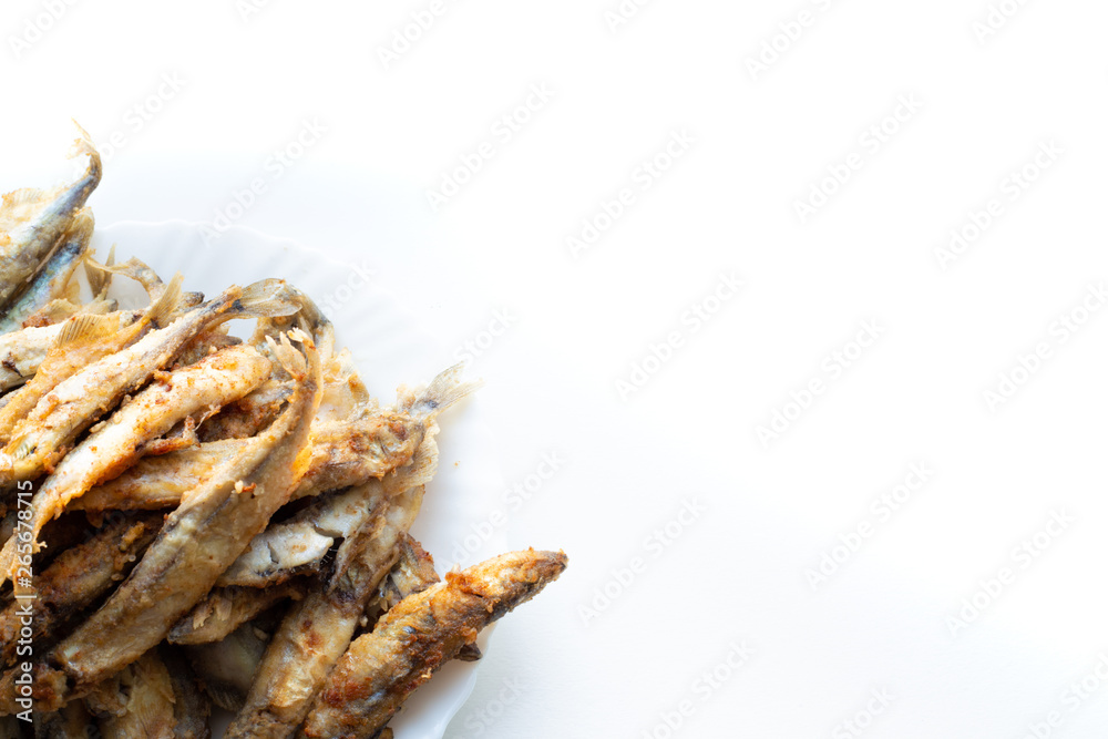white plate with fried capelin in the lower left corner on a white background white plate with fried capelin in the lower left corner on a white background