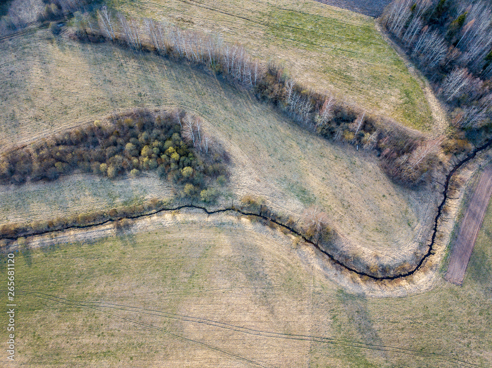 aerial view of small country river bed wavy in spring time in countryside