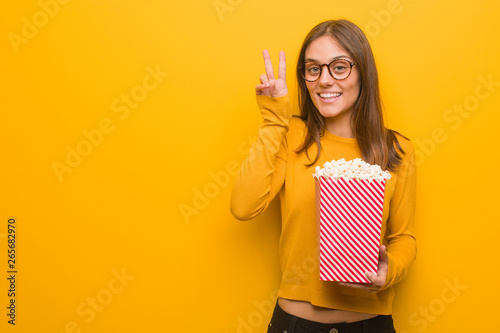 Young pretty caucasian woman fun and happy doing a gesture of victory. She is eating popcorns.