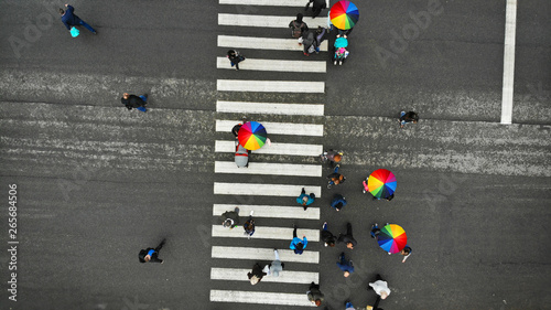 People crowd crossing a pedestrian crosswalk in a nasty day. Some of them with colorful umbrella. Top view. photo