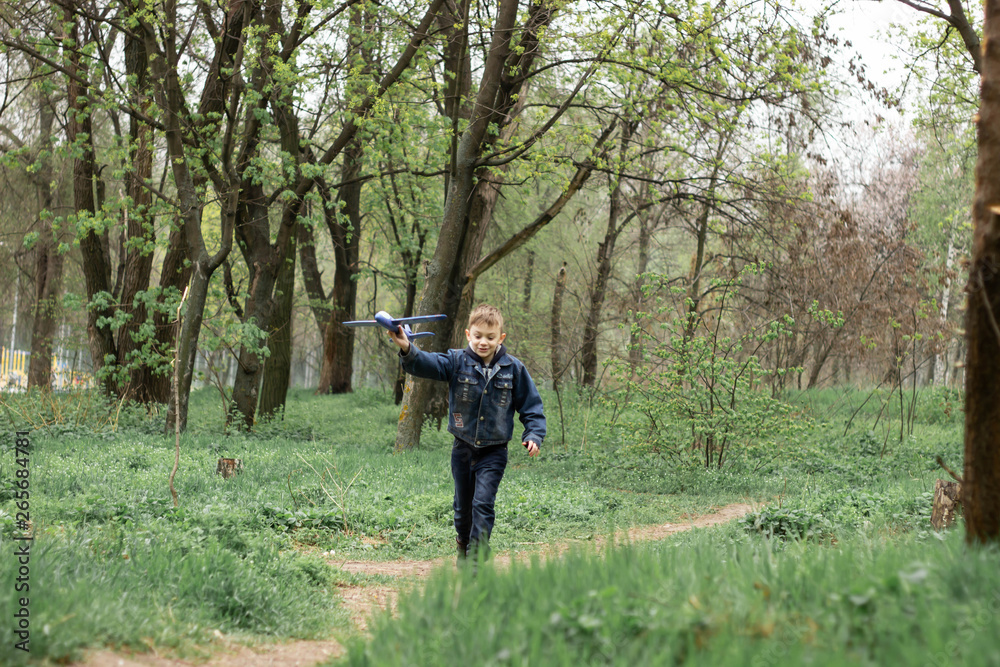 The boy launches a blue plane into the sky in a dense forest