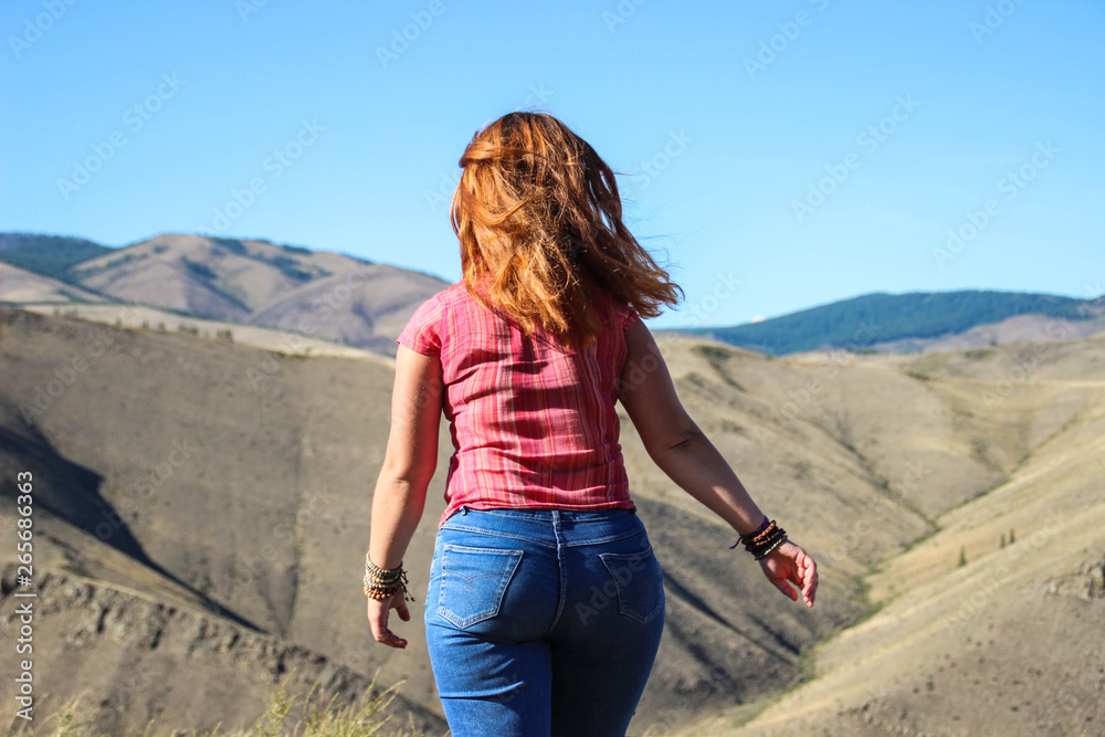 Chubby girl tourist with red hair in jeans in the mountains