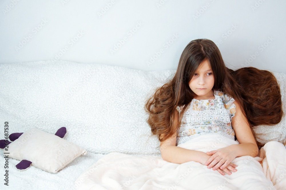 Home portrait of a little girl with long hair sitting on a couch covered with a blanket Home portrait of a little girl with long hair sitting on a couch covered with a blanket