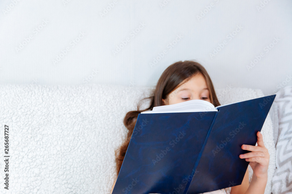 Home portrait of a little girl with long hair sitting in a bed and reading a book Home portrait of a little girl with long hair sitting in a bed and reading a book